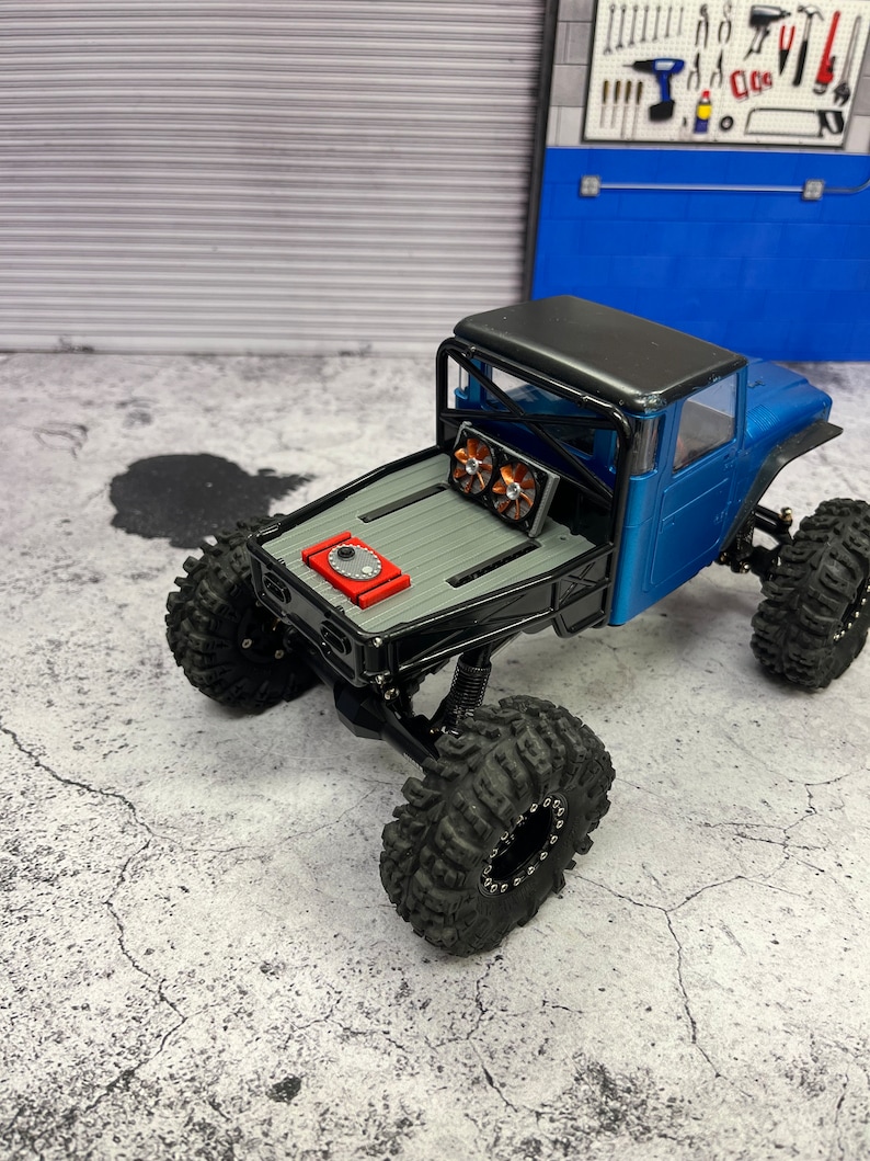 Pode incluir: Um caminh&atilde;o de brinquedo azul e preto com uma gaiola de seguran&ccedil;a preta e um motor vermelho. O caminh&atilde;o tem pneus grandes pretos e est&aacute; sentado em uma superf&iacute;cie de concreto cinza.