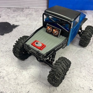 Pode incluir: Um caminh&atilde;o de brinquedo preto e azul com uma gaiola de seguran&ccedil;a preta e uma c&eacute;lula de combust&iacute;vel vermelha. O caminh&atilde;o tem pneus pretos e duas ventoinhas na parte traseira.