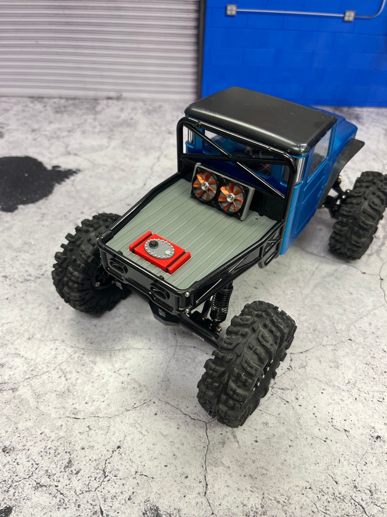 Pode incluir: Um caminh&atilde;o de brinquedo preto e azul com uma gaiola de seguran&ccedil;a preta e uma c&eacute;lula de combust&iacute;vel vermelha. O caminh&atilde;o tem pneus pretos e duas ventoinhas na parte traseira.