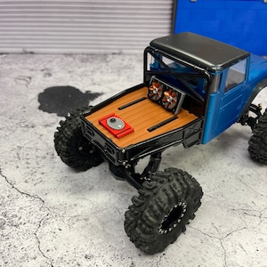 Pode incluir: Um caminh&atilde;o de brinquedo azul e preto com uma cama de madeira e uma c&eacute;lula de combust&iacute;vel vermelha. O caminh&atilde;o tem pneus pretos e uma gaiola de rolagem preta. O caminh&atilde;o est&aacute; sentado em uma superf&iacute;cie de concreto cinza.