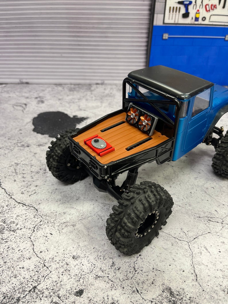 Pode incluir: Um caminh&atilde;o de brinquedo azul e preto com uma cama de madeira e uma c&eacute;lula de combust&iacute;vel vermelha. O caminh&atilde;o tem pneus pretos e uma gaiola de rolagem preta. O caminh&atilde;o est&aacute; sentado em uma superf&iacute;cie de concreto cinza.