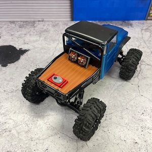 Pode incluir: Um caminh&atilde;o de brinquedo azul e preto com uma ca&ccedil;amba de madeira e rodas pretas. O caminh&atilde;o tem uma gaiola de seguran&ccedil;a preta e dois ventiladores na parte traseira.