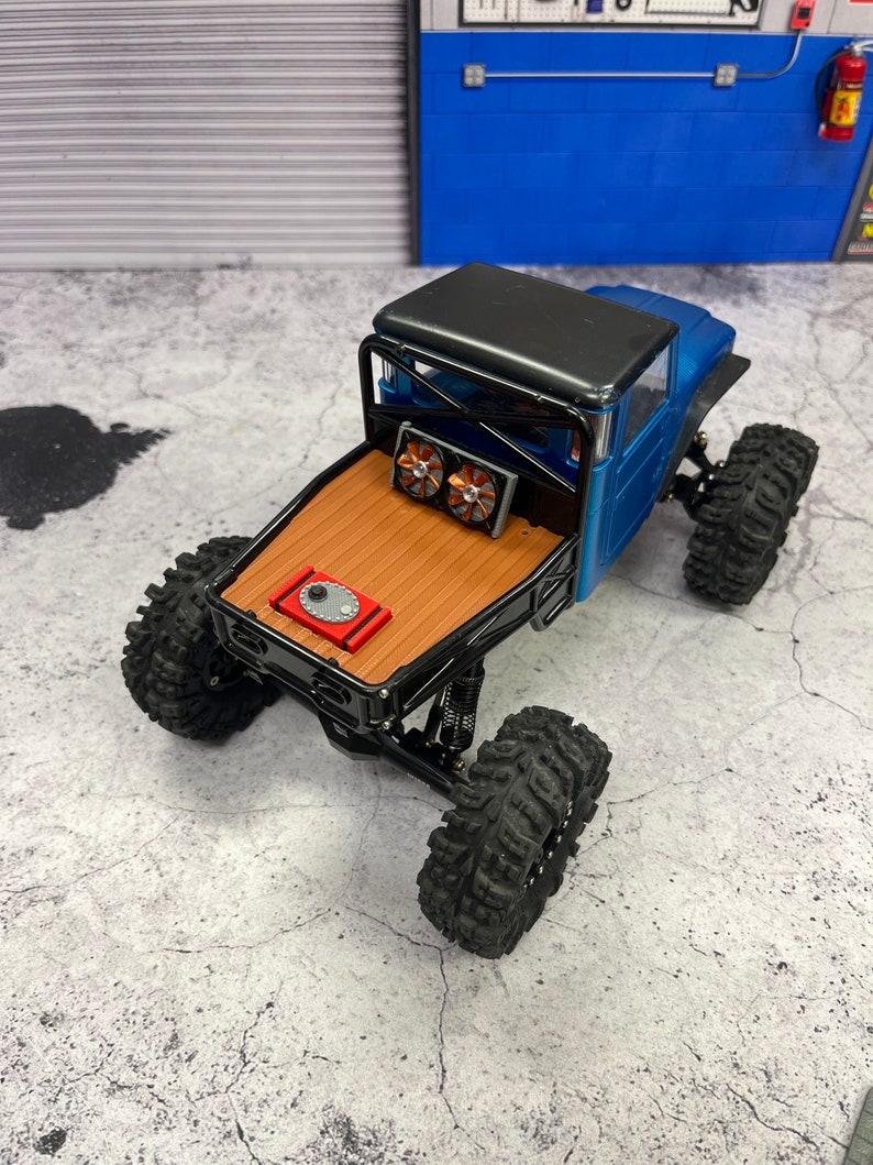 Pode incluir: Um caminh&atilde;o de brinquedo azul e preto com uma ca&ccedil;amba de madeira e rodas pretas. O caminh&atilde;o tem uma gaiola de seguran&ccedil;a preta e dois ventiladores na parte traseira.