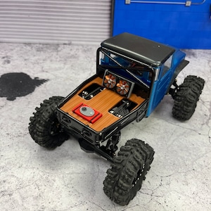 Pode incluir: Um caminh&atilde;o de brinquedo azul e preto com uma ca&ccedil;amba de madeira e dois ventiladores na parte de tr&aacute;s. O caminh&atilde;o est&aacute; sentado em uma superf&iacute;cie de concreto cinza.