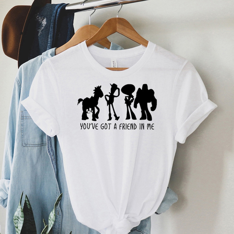 May include: White t-shirt with a black silhouette of the Toy Story characters Woody, Buzz Lightyear, Jessie, and Bullseye. The text "You've got a friend in me" is printed below the characters.