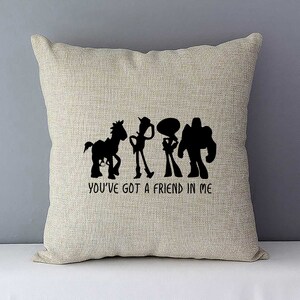May include: A beige throw pillow with a black silhouette of the Toy Story characters Woody, Buzz Lightyear, Jessie, and Bullseye. The text "You've got a friend in me" is printed below the characters.
