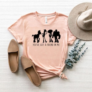 May include: A pink t-shirt with a black silhouette of the Toy Story characters Woody, Buzz Lightyear, and Bullseye. The text "You've got a friend in me" is printed below the characters.