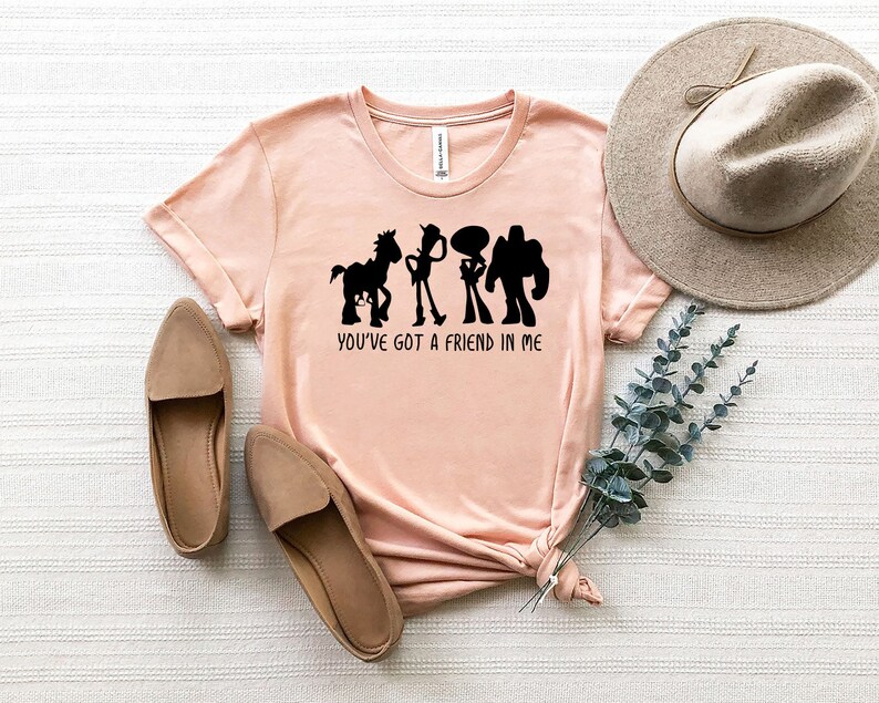 May include: A pink t-shirt with a black silhouette of the Toy Story characters Woody, Buzz Lightyear, and Bullseye. The text "You've got a friend in me" is printed below the characters.