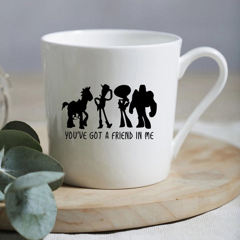 May include: White ceramic mug with a black silhouette of the Toy Story characters Woody, Buzz Lightyear, Jessie, and Bullseye. The text "You've got a friend in me" is printed below the characters.