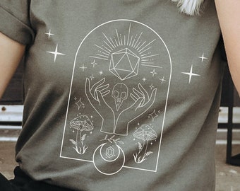 May include: A green t-shirt with a white graphic design featuring a skull, two hands, a geometric shape, and mushrooms. The design is surrounded by a white arch and stars.