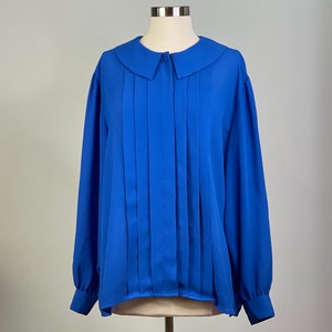 Könnte beinhalten: Eine langärmelige Bluse in Königsblau mit einer plissierten Vorderseite und einem großen, weißen Kragen. Die Bluse hat eine Knopfleiste vorne.