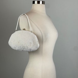 May include: A white beaded evening bag with a silver clasp. The bag is oval shaped and has a short strap.