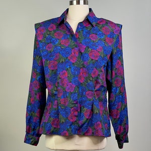 Könnte beinhalten: Eine langärmelige, geknöpfte Bluse mit einem Blumendruck mit blauen, rosa und roten Rosen auf einem dunkelgrünen Hintergrund.