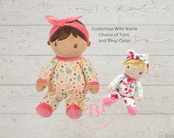 Puede incluir: Dos muñecas de peluche, una grande y otra pequeña, ambas con pijamas florales y cintas para la cabeza a juego. La muñeca más grande tiene el pelo castaño y una cinta rosa. La muñeca más pequeña tiene el pelo rubio y el nombre "Mary Kate" en el frente. El texto en la imagen dice "Personaliza con nombre, elección de fuente y color de vinilo."
