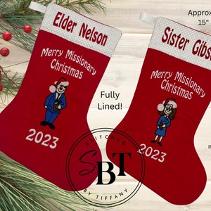 May include: Two red Christmas stockings with white trim. The stockings are personalized with the names "Elder Nelson" and "Sister Gibson" and the text "Merry Missionary Christmas". Each stocking has the year "2023" embroidered on the front. The stockings are approximately 15 inches by 10 inches.