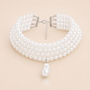 May include: A white pearl choker necklace with multiple strands and a silver clasp. The necklace features a large, irregular-shaped pearl pendant. The pearls are round and evenly spaced, creating a classic and elegant look.