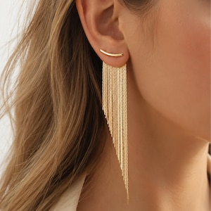 May include: A gold-toned ear climber earring featuring a curved bar that rests along the earlobe, with multiple delicate, dangling chain strands of varying lengths extending downward to create an asymmetrical, layered fringe effect.