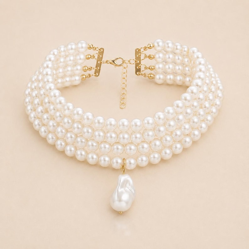 May include: A multi-strand pearl choker necklace with a gold-tone clasp and a large, irregular pearl pendant. The necklace features five strands of round, white pearls. The clasp and connecting elements are gold-colored.