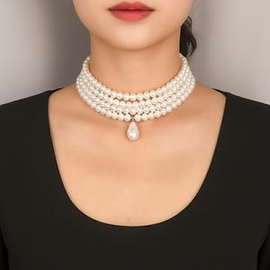 May include: A multi-strand pearl choker necklace with a pear-shaped pendant. The necklace features four rows of round, white pearls. The pendant hangs from the center of the necklace and is also a white pearl.