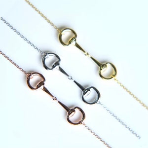 May include: Three delicate necklaces featuring a horse bit design. The necklaces are silver, gold, and rose gold.