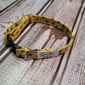 May include: Yellow dog collar with a floral pattern and a silver buckle. The collar has a white tag that says "Annie Rae Small Co."