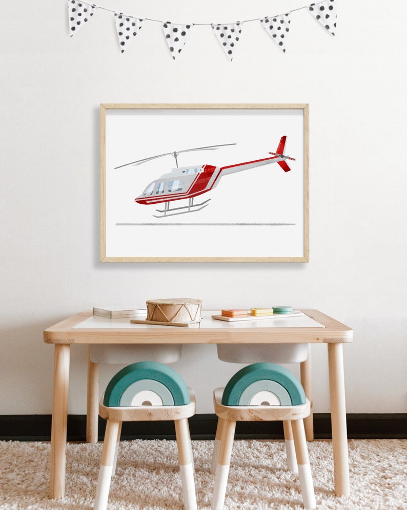 May include: A framed print of a red and white helicopter against a white background. The print is hanging on a white wall above a wooden table with two teal rainbow-shaped chairs.
