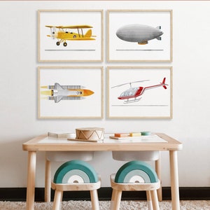 May include: Four framed illustrations of different types of aircraft, including a yellow biplane, a gray blimp, a white space shuttle, and a red helicopter. The frames are hanging on a white wall above a wooden table with two teal and white rainbow-shaped chairs.