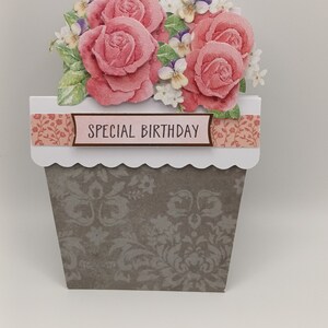 May include: A handmade card featuring a pop-up bouquet of pink roses and white flowers in a brown pot. The card has a scalloped edge and a banner that reads "SPECIAL BIRTHDAY".