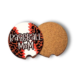May include: A round, white, cork-backed coaster with a red and black leopard print design. The coaster features a baseball graphic with the text "Baseball Mom" in black.