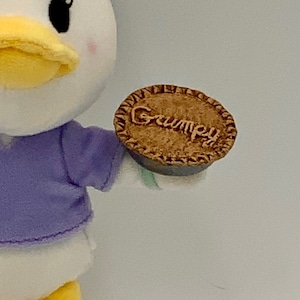 May include: A plush toy duck holding a brown pie with the word "Grumpy" written on it.