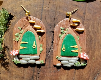 May include: A pair of green door earrings with mushroom and stone accents. The earrings are made of polymer clay and have a rustic, whimsical style.
