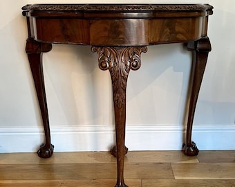 May include: A dark wood console table with a carved top and three legs. The legs are carved with a claw foot design.