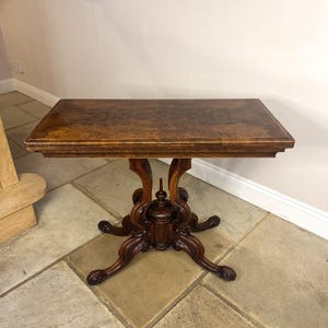 May include: An antique rectangular table in dark wood. The table has an ornate base with curved legs and a decorative central support. The tabletop features a patterned design. The table is approximately 76 cm long.