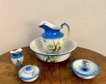 May include: A vintage porcelain wash set comprising a jug, basin, small jug, lidded dish, and soap dish. The set has a white base with blue trim and is decorated with colourful bird and floral motifs. The jug and basin are the largest pieces.