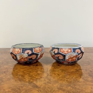 Könnte beinhalten: Zwei kleine, dekorative Schalen mit geometrischem Muster. Die Schalen sind aus weißer Keramik und mit blauen, roten und goldenen geometrischen Mustern verziert. Die Schalen stehen auf einer Holzoberfläche.