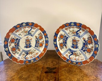 May include: Two large, round, white porcelain plates with blue and red floral designs. The plates have a scalloped edge and are decorated with a central motif of a vase with flowers.