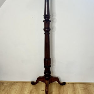 May include: A dark brown wooden plant stand with a round top and three legs. The stand has a decorative design on the column.