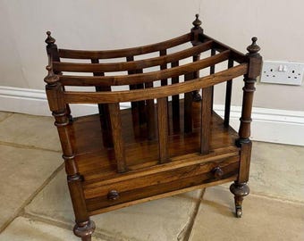 May include: A dark wood magazine rack with a drawer and castors. The rack has a curved top and decorative finials.