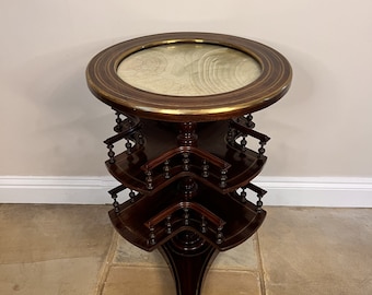 May include: A three-tiered mahogany revolving table with a round top and brass trim. The table has a light wood top and a dark wood base.