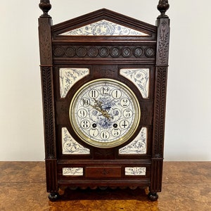 May include: A dark wood antique clock with a white porcelain face and blue floral accents. The clock has a decorative carved frame and a Roman numeral clock face.