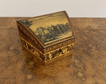 May include: A small wooden box with a hinged lid. The lid is decorated with a black and white image of a castle. The box is made of wood with a marquetry design. The box has a small keyhole on the front.