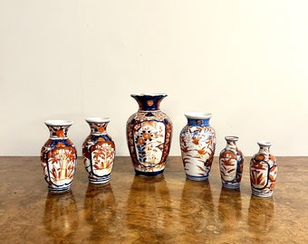 May include: A set of six porcelain vases with blue and white floral designs. The vases are arranged in a row on a wooden surface. The largest vase is in the centre and the smallest vases are at either end.