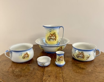 May include: A set of vintage ceramic housewares, including two handled bowls, a jug, a small bowl, a small vase, and a large bowl. Each piece features a blue and yellow landscape design. The items are arranged on a wooden table.