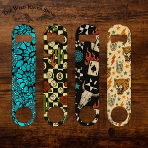 May include: Four metal bottle openers with unique designs. One features turquoise floral patterns, another has a checkerboard with dice and cacti, the third has a skull and playing cards, and the last has a leopard and lightning bolts. The Wild Raven Shop logo is at the top.