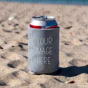 Könnte beinhalten: Ein grauer Getränkedosenkühler mit dem weißen Text "YOUR IMAGE HERE", der eine silberne und rote Dose hält. Der Kühler befindet sich an einem Sandstrand, mit dem Meer im Hintergrund.