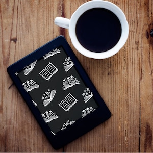 May include: A black e-reader with a white pattern of open books and stars on the screen. A cup of coffee is in the background.