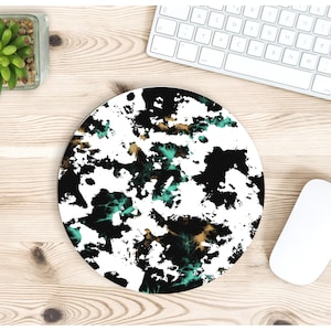 May include: A round mouse pad with a black, white, teal, and gold abstract design. The design resembles a splattered paint effect.