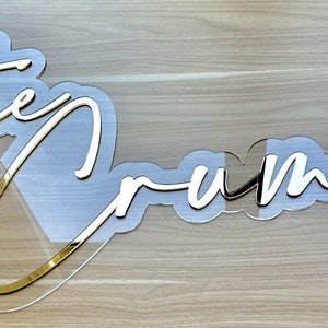 May include: Gold acrylic sign with the words "the dreams" in a cursive font.