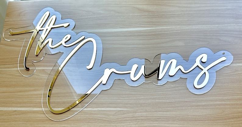 May include: Gold acrylic sign with the words "the dreams" in a cursive font.