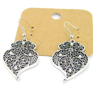 May include: A pair of silver filigree earrings with a heart shape and small clear rhinestones.
